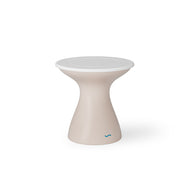 The Autograph Tall Ice Bin Side Table by Ledge Lounger is a beige, hourglass-shaped stool with a modern design and round white top, perfect as an outdoor side table. A small blue logo at the bottom adds charm against the white backdrop.