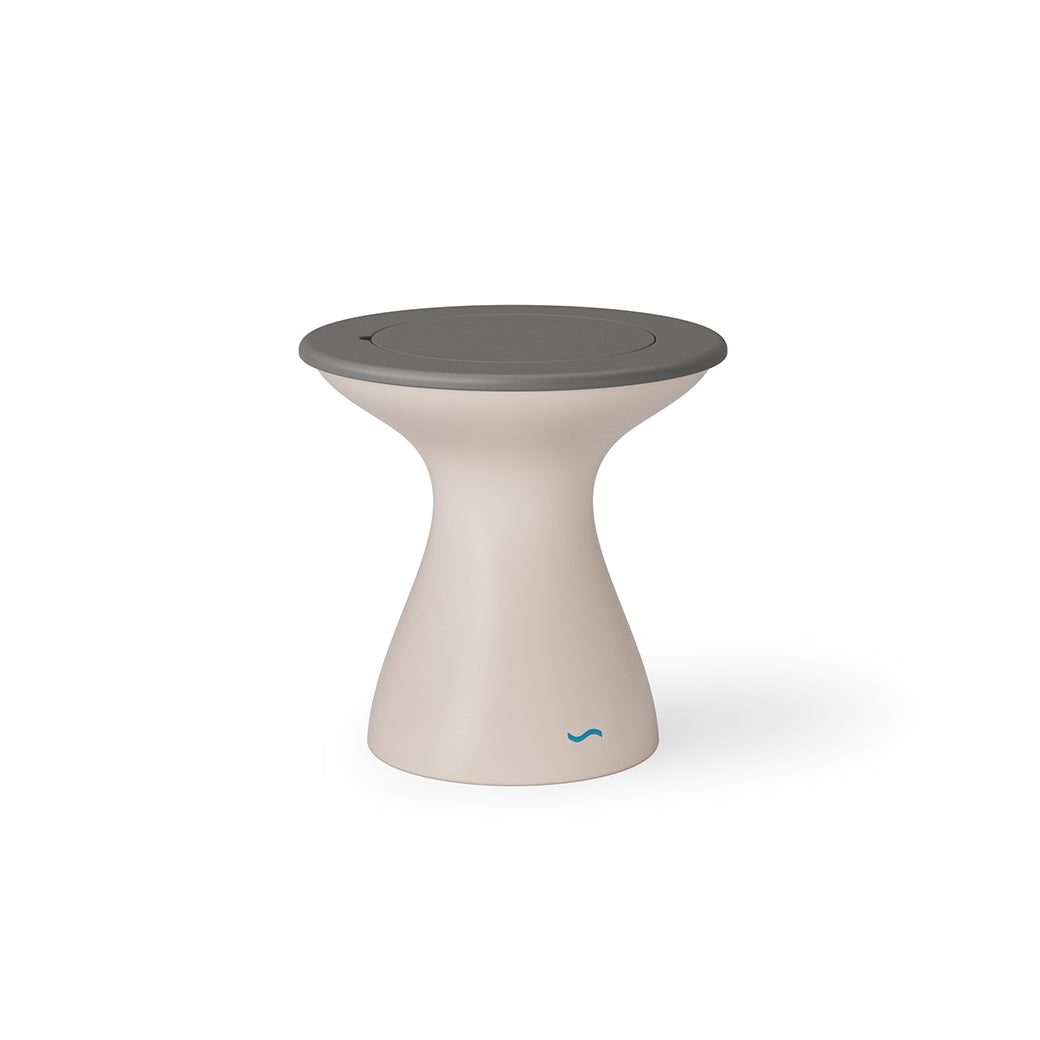 The Autograph Tall Ice Bin Side Table by Ledge Lounger is a modern, hourglass-shaped stool that also serves as a chic outdoor side table. It features a beige body, flat round gray top, and sleek minimalist design with a small blue logo near the base.