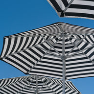 Ledge Loungers 7.5 Octagon Signature 360° Tilt Umbrella boasts black and white stripes and resort-level luxury, open against a clear blue sky. Viewed from below, it highlights geometric patterns with fabric and metal frames, elevating any outdoor space into a sophisticated retreat.