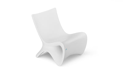 The Autograph Chair by Ledge Lounger is a modern, minimalist white chair with smooth contours and a low seat, featuring a futuristic design. Its seamless ergonomic form rests on two wide, angled legs, ideal for relaxing in luxurious outdoor settings.
