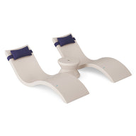 The Ledge Lounger Signature Chaise Headrest Pillow and Side Table In-Pool Set features two modern beige chaises with navy headrests, joined by a round table, all displayed against a white background.