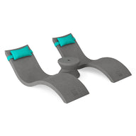 The Ledge Lounger Signature Chaise Headrest Pillow and Side Table In-Pool Set features double gray loungers with teal pillows and a small round table, creating an ideal outdoor paradise on a white backdrop.