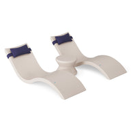 The Ledge Lounger Signature Chaise Headrest Pillow and Side Table In-Pool Set features two modern curved beige loungers with blue headrest pillows, connected by a round side table, creating a stylish poolside seating arrangement.