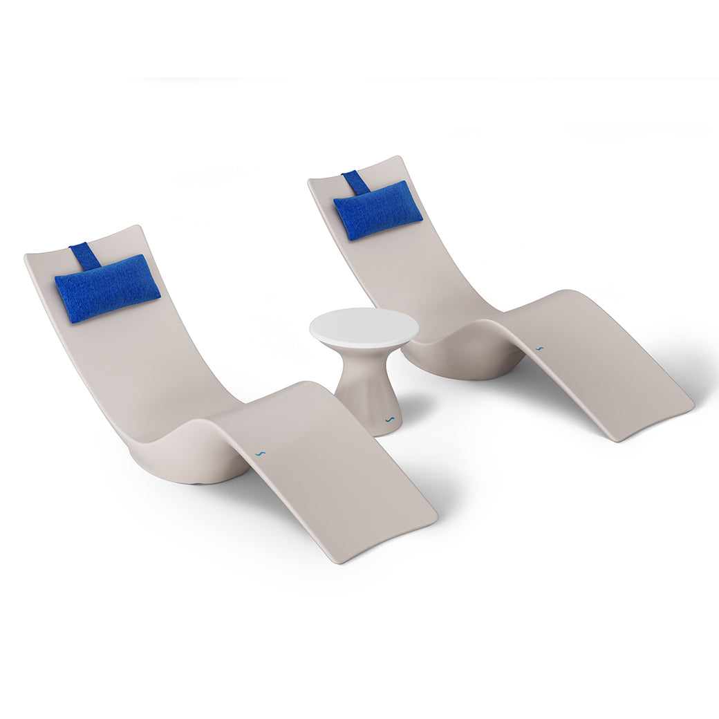 The Resort Luxury Outdoor Paradise In-Pool Furniture Bundle by Ledge Lounger features two modern beige chaise loungers with blue headrests and a small white round table, creating a minimalist poolside arrangement perfectly set against a plain white background.