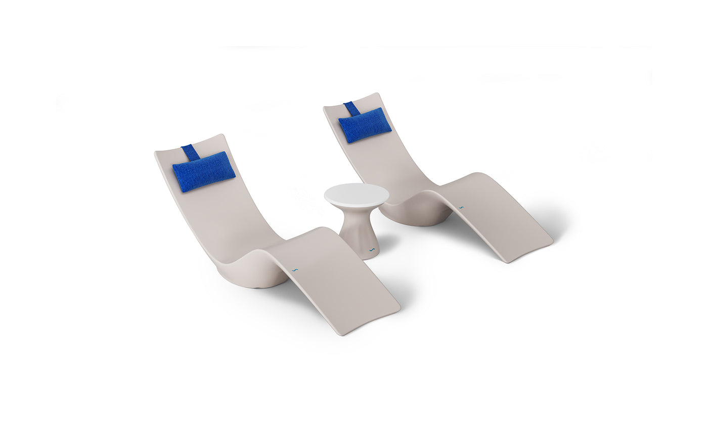 The Resort Luxury Outdoor Paradise In-Pool Furniture Bundle by Ledge Lounger features two modern beige chaise loungers with blue headrests and a small white round table, creating a minimalist poolside arrangement perfectly set against a plain white background.