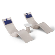 Two beige chaise loungers with blue headrests and a small, round white table create a minimalist, stylish setup ideal for poolside relaxation. Enjoy this aesthetic with the Resort Luxury Outdoor Paradise In-Pool Furniture Bundle from Ledge Lounger.