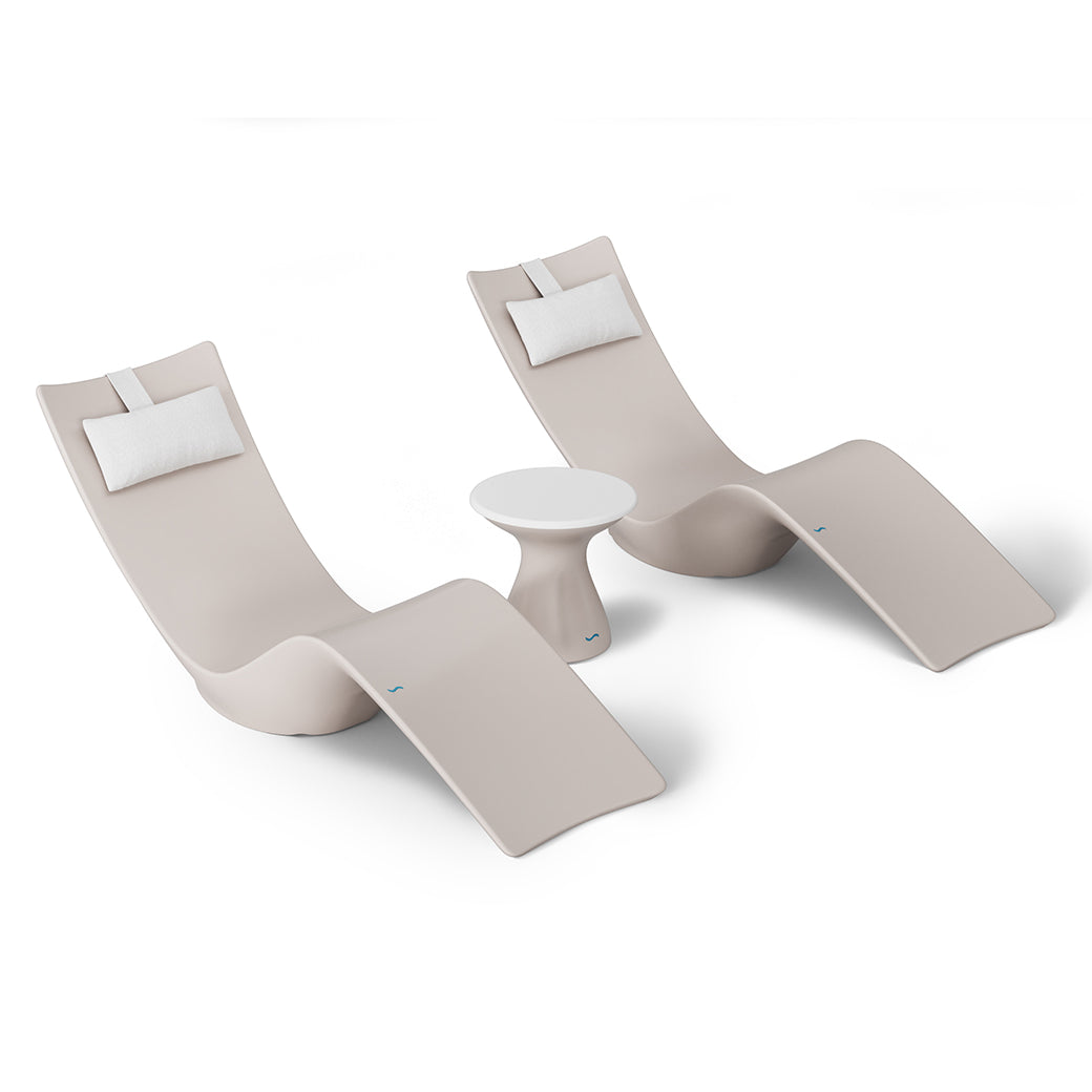 The Resort Luxury Outdoor Paradise In-Pool Furniture Bundle by Ledge Lounger includes two beige, modern lounge chairs with white pillows and a small round white table, offering a sleek, curved design perfect for poolside relaxation. The minimalist style is highlighted against a white background.