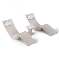 The Resort Luxury Outdoor Paradise In-Pool Furniture Bundle by Ledge Lounger includes two beige, modern lounge chairs with white pillows and a small round white table, offering a sleek, curved design perfect for poolside relaxation. The minimalist style is highlighted against a white background.