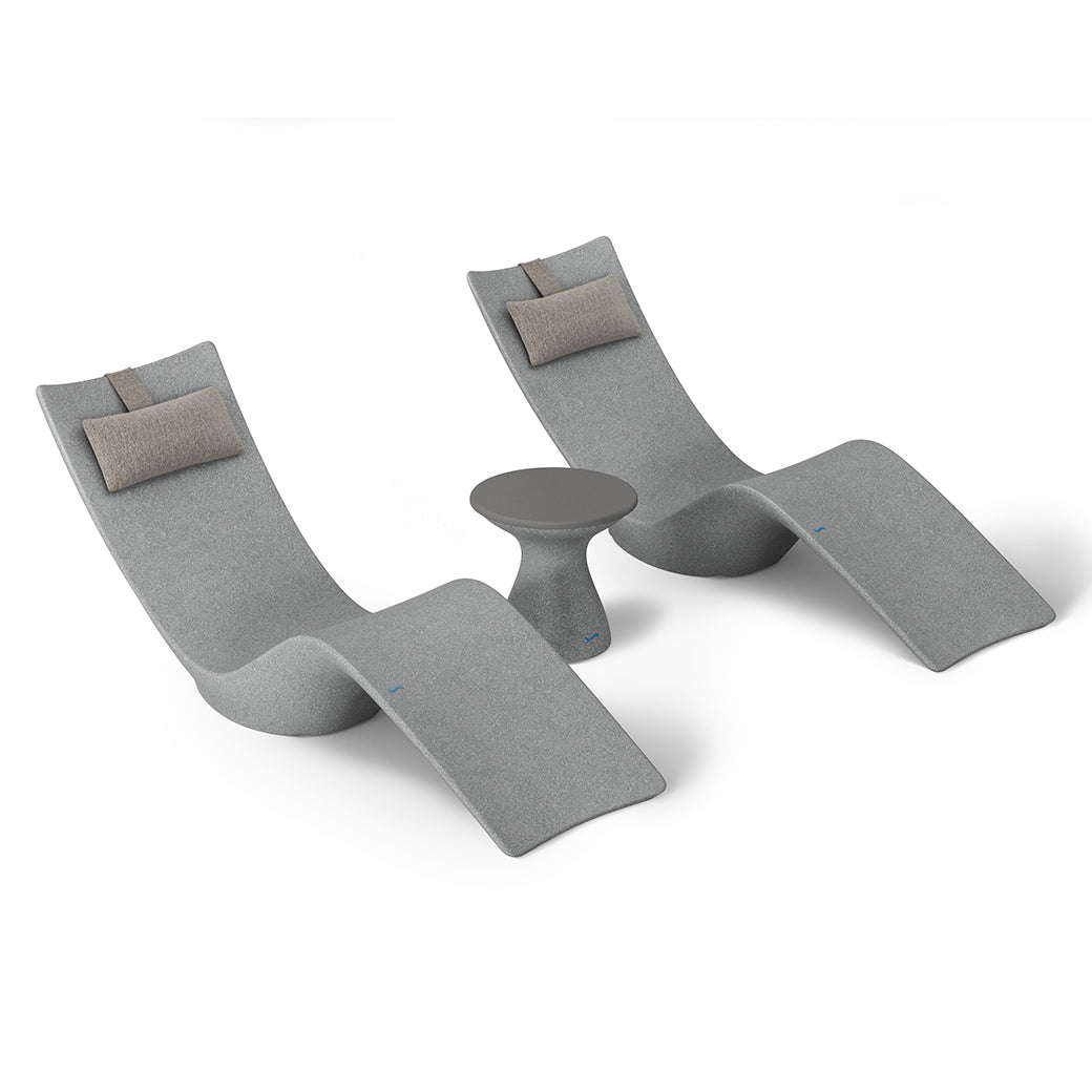 Two curved lounge chairs with light gray upholstery and beige headrests from the Resort Luxury Outdoor Paradise In-Pool Furniture Bundle by Ledge Lounger, flank a small round gray side table, offering a serene poolside vibe against a plain white backdrop.