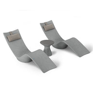 Two curved lounge chairs with light gray upholstery and beige headrests from the Resort Luxury Outdoor Paradise In-Pool Furniture Bundle by Ledge Lounger, flank a small round gray side table, offering a serene poolside vibe against a plain white backdrop.