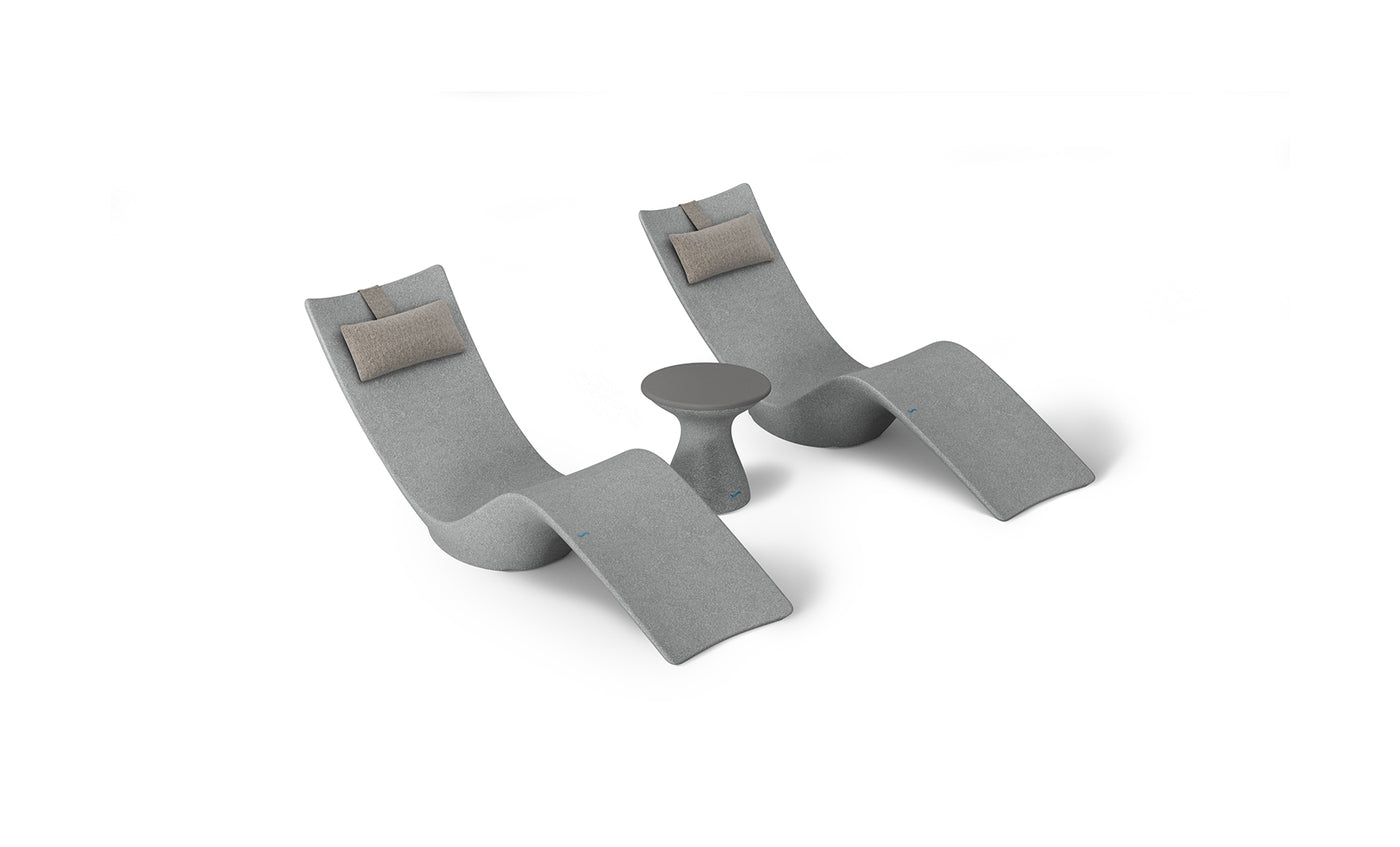 Two curved lounge chairs with light gray upholstery and beige headrests from the Resort Luxury Outdoor Paradise In-Pool Furniture Bundle by Ledge Lounger, flank a small round gray side table, offering a serene poolside vibe against a plain white backdrop.