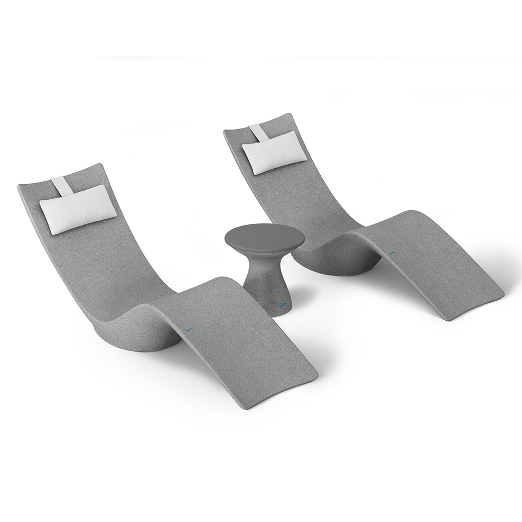 The Resort Luxury Outdoor Paradise In-Pool Furniture Bundle by Ledge Lounger features two modern chaise loungers with gray upholstery and white headrest cushions, flanking a small round gray side table, ideal for poolside relaxation. The set is displayed against a plain white background.