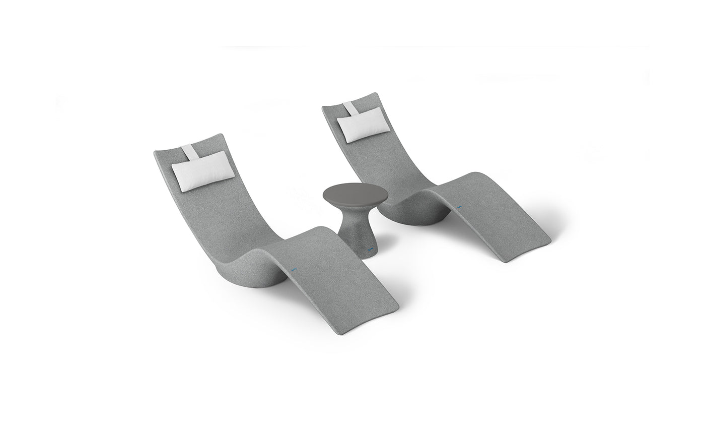 The Resort Luxury Outdoor Paradise In-Pool Furniture Bundle by Ledge Lounger features two modern chaise loungers with gray upholstery and white headrest cushions, flanking a small round gray side table, ideal for poolside relaxation. The set is displayed against a plain white background.