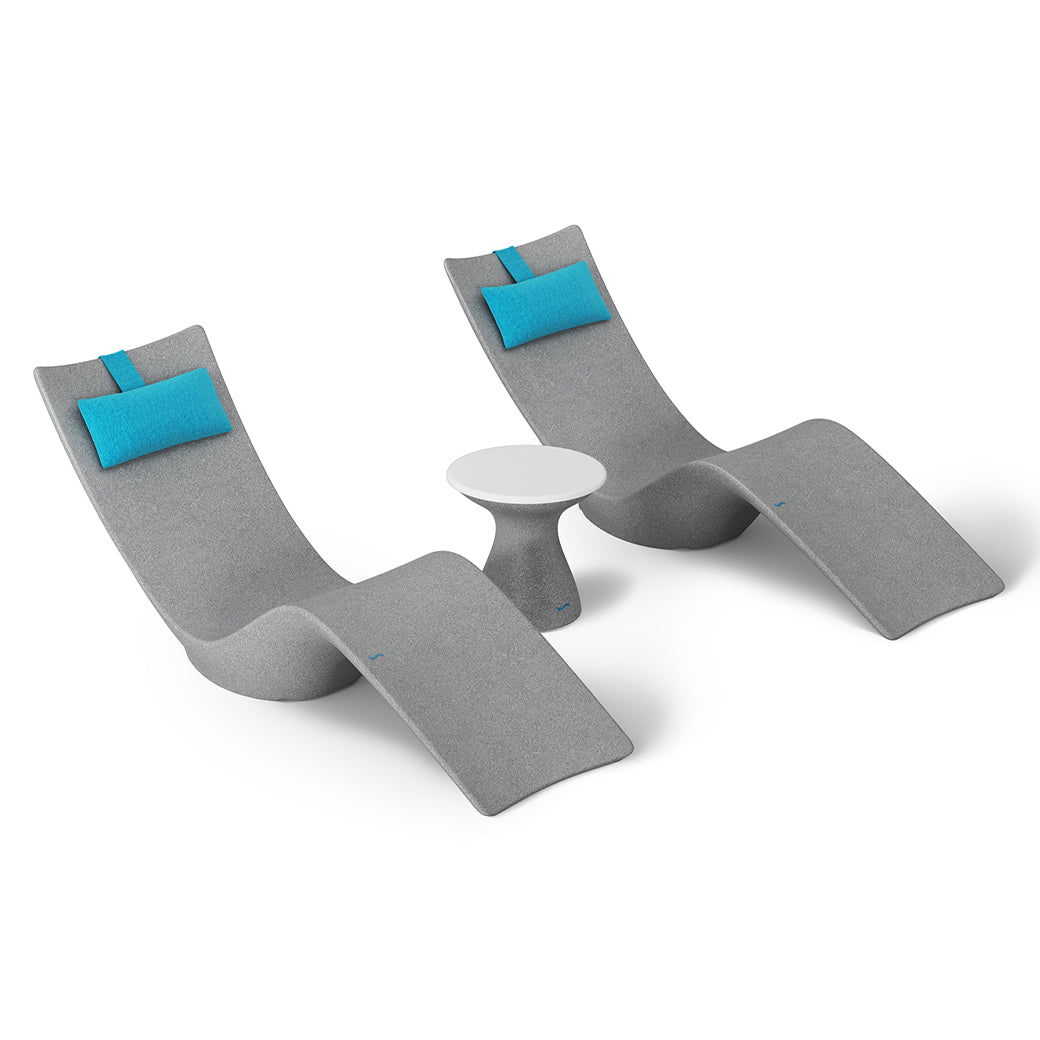 The Resort Luxury Outdoor Paradise In-Pool Furniture Bundle by Ledge Lounger features two modern gray chaise loungers with blue headrests and a small round table, creating a contemporary, minimalist style perfect for poolside relaxation.