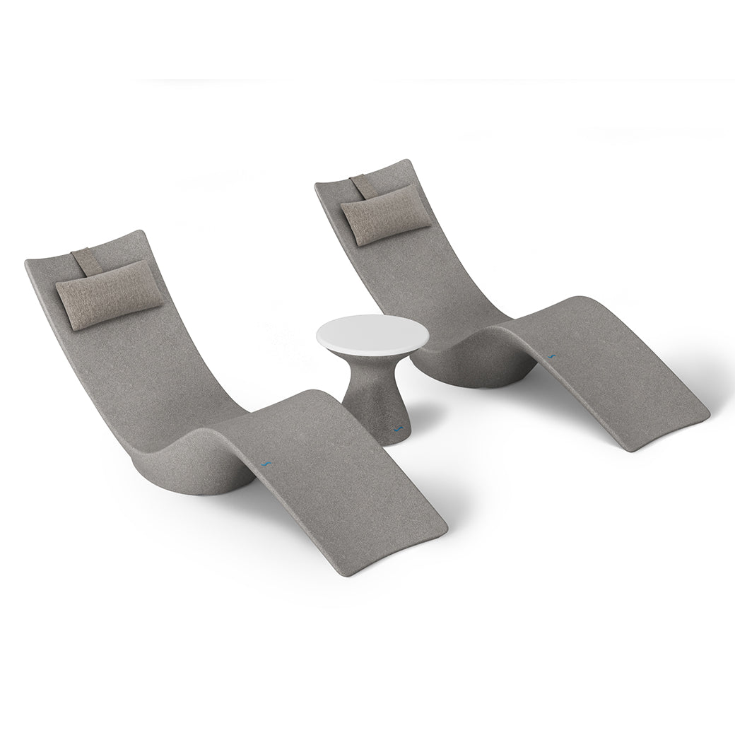 The Resort Luxury Outdoor Paradise In-Pool Furniture Bundle by Ledge Lounger includes two sleek, modern chaise loungers in minimalist gray with beige headrests, arranged beside a small round white side table. This elegant setup, perfect for poolside relaxation, is displayed against a plain white background.