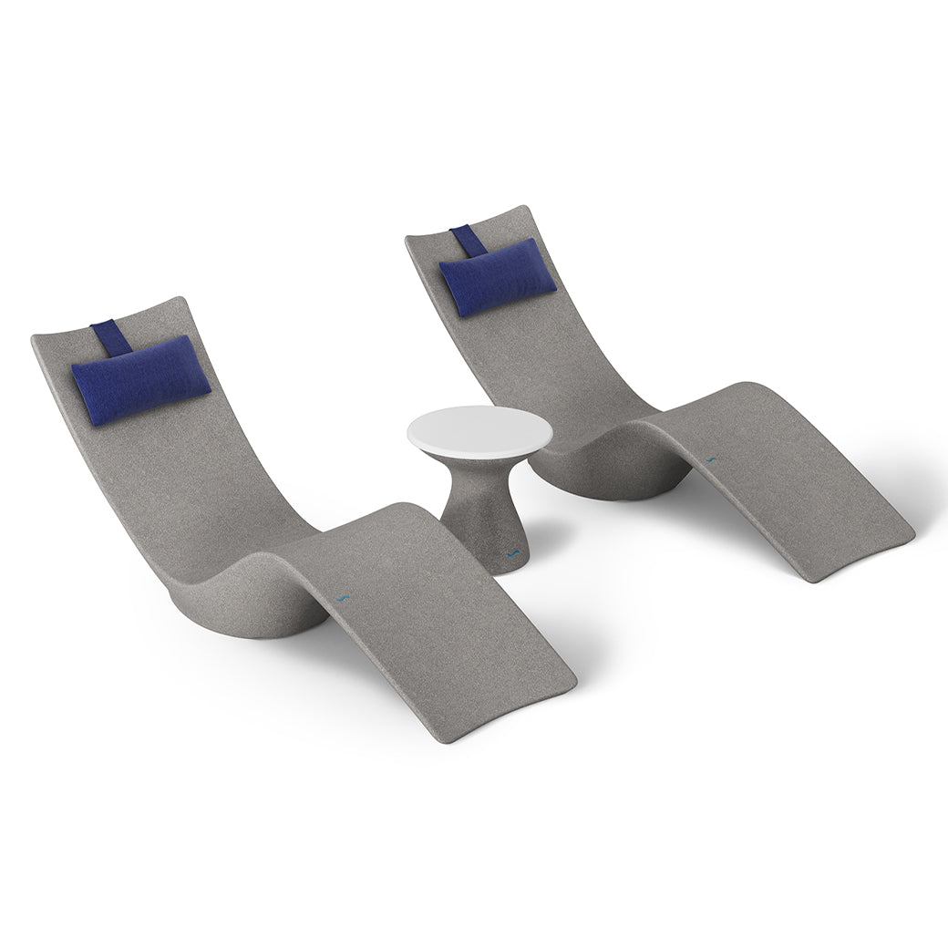The Resort Luxury Outdoor Paradise In-Pool Furniture Bundle by Ledge Lounger features two modern gray chaise lounger-style chairs with dark blue cushions, flanking a small round white table, offering sleek, curved design perfect for poolside relaxation with minimalist allure.