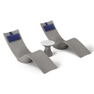 The Resort Luxury Outdoor Paradise In-Pool Furniture Bundle by Ledge Lounger features two modern gray chaise lounger-style chairs with dark blue cushions, flanking a small round white table, offering sleek, curved design perfect for poolside relaxation with minimalist allure.