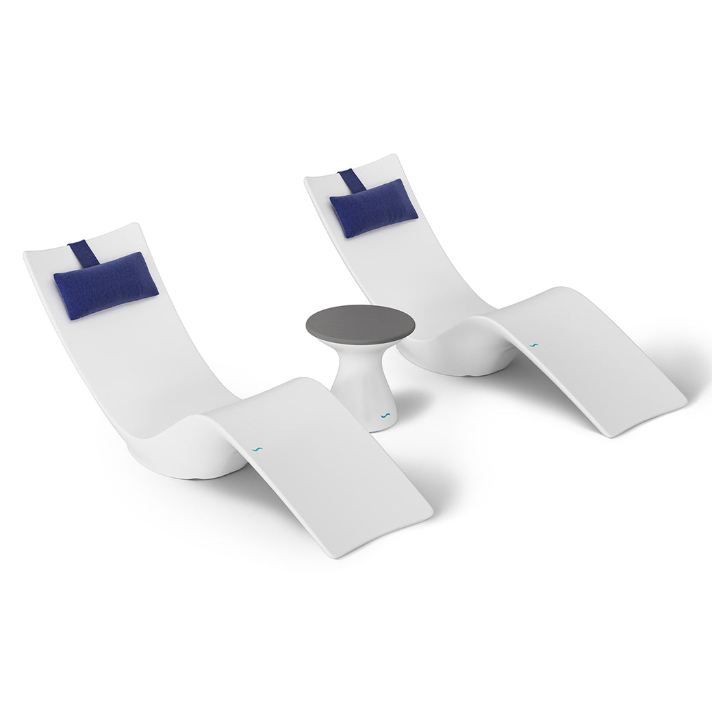 The Resort Luxury Outdoor Paradise In-Pool Furniture Bundle by Ledge Lounger features two modern white chaise loungers with blue headrests side by side and a small round table with a gray top, ideal for poolside relaxation, all set against a minimalist white background.