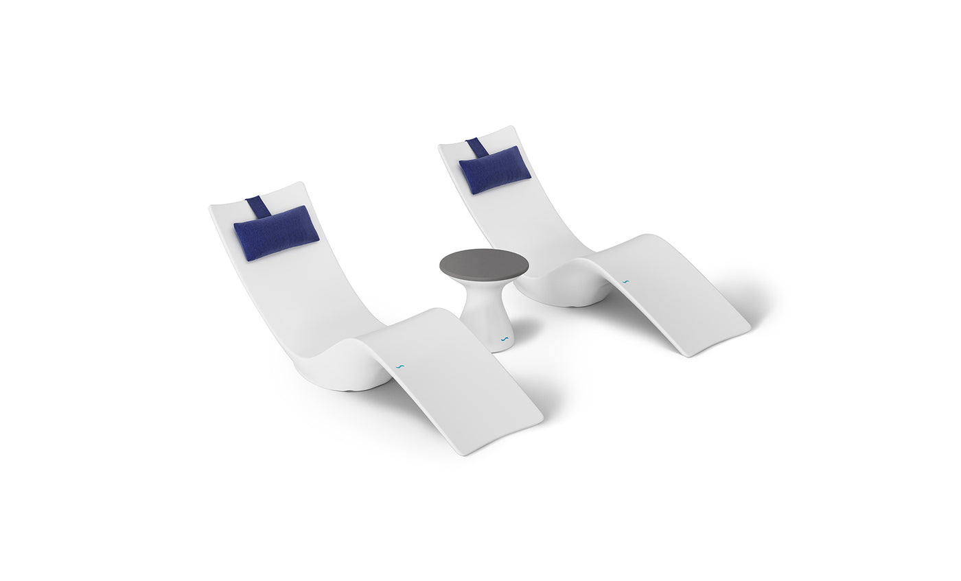 The Resort Luxury Outdoor Paradise In-Pool Furniture Bundle by Ledge Lounger features two modern white chaise loungers with blue headrests side by side and a small round table with a gray top, ideal for poolside relaxation, all set against a minimalist white background.