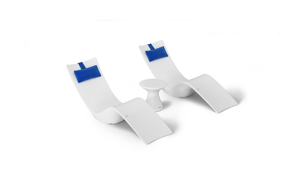 The Resort Luxury Outdoor Paradise In-Pool Furniture Bundle by Ledge Lounger features two modern white lounge chairs with blue head cushions flanking a small white table, ideal for poolside relaxation against a plain white backdrop to highlight its sleek and minimalist design.