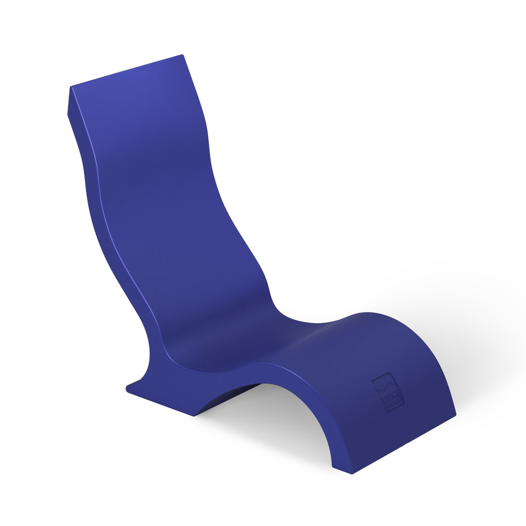 The Ledge Lounger Signature Chair is a modern, abstract piece featuring a curvy, S-like design in deep blue. Its durable construction offers a high backrest and wavy seat, making it ideal for stylish poolside seating against a plain white background.