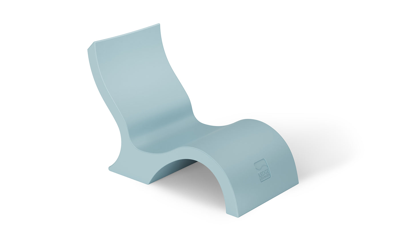 The Ledge Lounger Signature Lowback Chair With Short Riser is a modern light blue molded lounger with smooth curves and an arched base, perfect for poolside seating and striking against a plain white background.