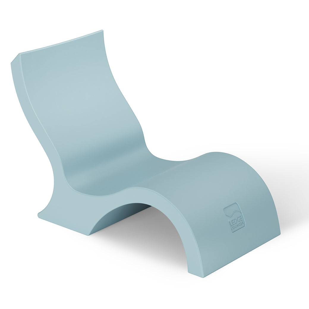 The Signature Lowback Chair from Ledge Lounger is a modern, light blue lounge chair with a sleek, curved design and smooth surface, ideal poolside seating for your outdoor oasis, set against a plain white background.