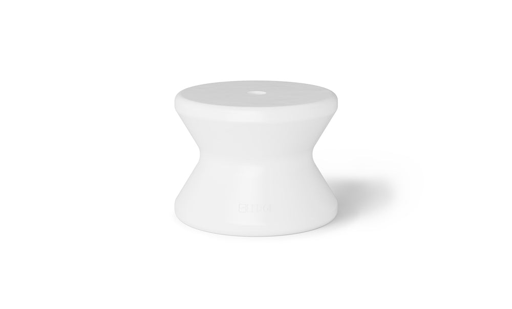 A sleek white, hourglass-shaped stool with a glossy finish is displayed on a white background. With its narrower middle and flat top, it complements the Ledge Lounger Signature Standard Side Table, making it perfect for sun shelf placement or in-pool use.