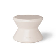 The Signature Standard Side Table by Ledge Lounger is a small, hourglass-shaped, light beige stool with a smooth surface for in-pool use on sun shelves. It features the word EDGE inscribed near the bottom, adding elegance and functionality.