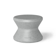 The Signature Standard Side Table by Ledge Lounger is a gray hourglass-shaped stool with a textured surface and smooth, curved design, perfect for in-pool use. The name BLØK is subtly engraved near the base, set against a plain white background.