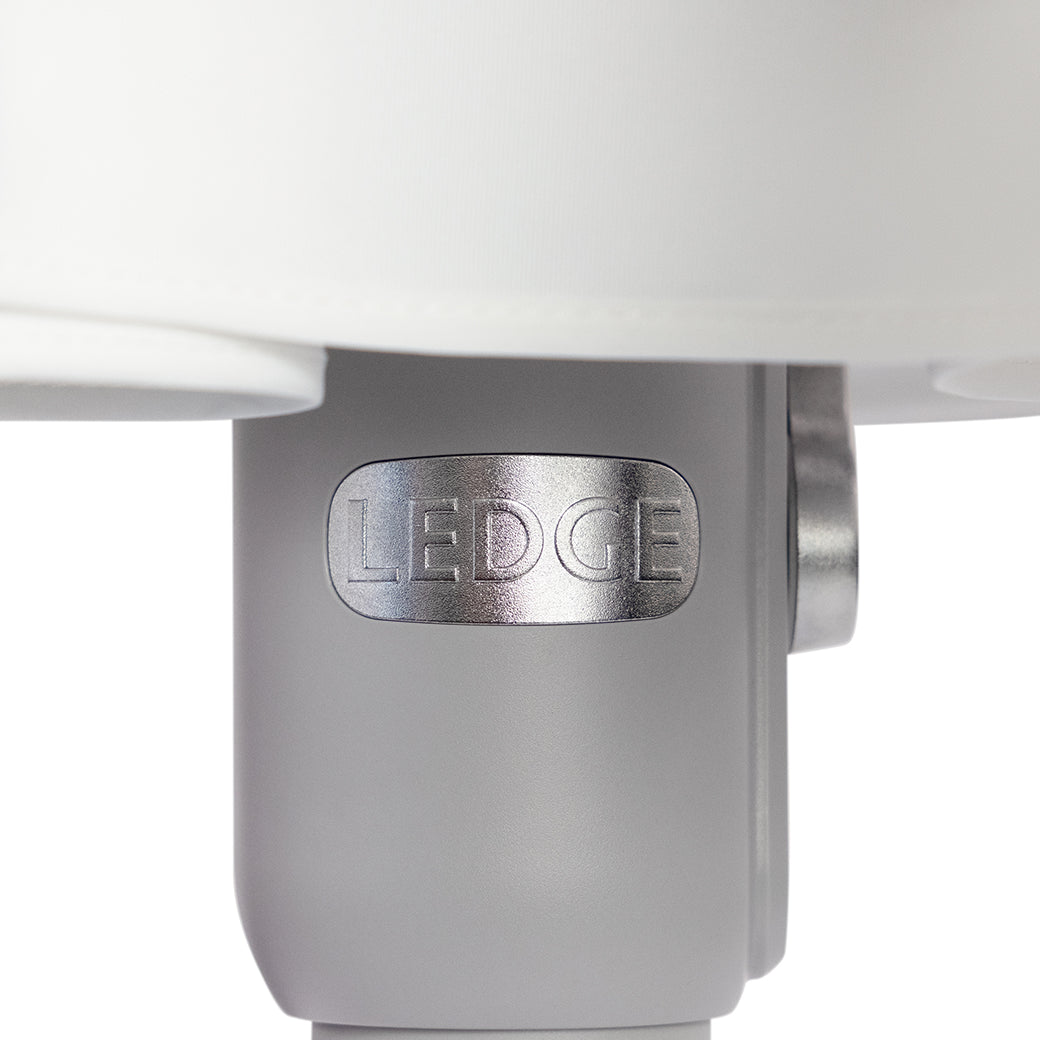 A close-up of a cylindrical metal component embossed with LEDCE evokes the durability of wind-resistant umbrellas. Connected to a larger white structure, it boasts a smooth light gray surface, reminiscent of the 6.5 Square Signature 360° Tilt Umbrella by Ledge Lounger.