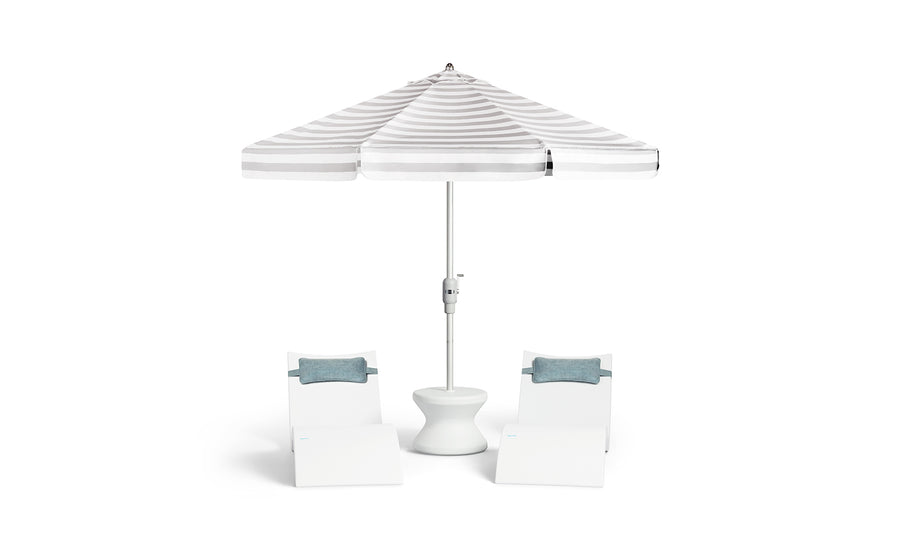 Two white lounge chairs with blue cushions flank a small white table, all shaded by the Ledge Lounger 7.5' Octagon Signature 360° Tilt Umbrella in classic white and gray stripes.