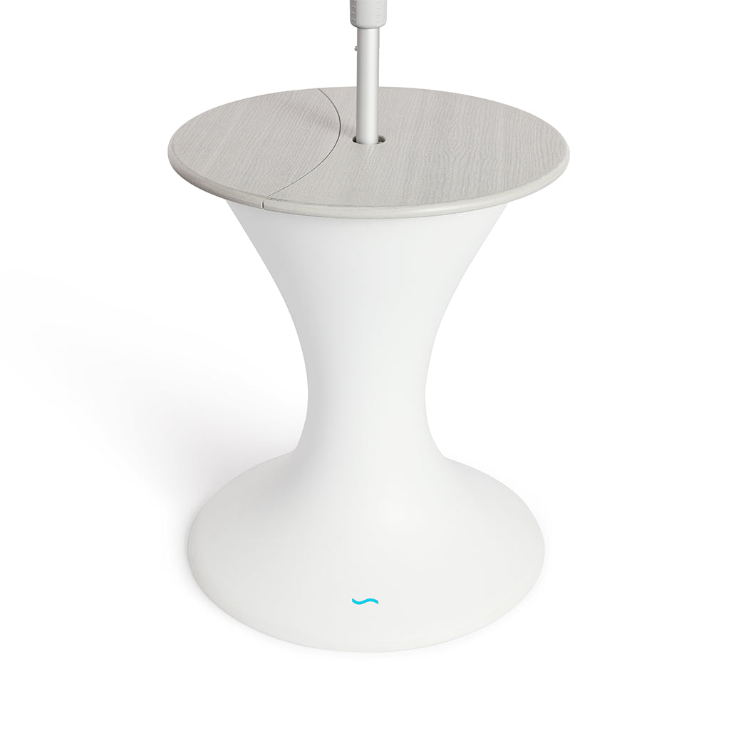 The Autograph Umbrella Stand Ice Bin by Ledge Lounger features a sleek design with a modern white pedestal base, a round gray top, and a central pole resembling an outdoor table. The flared base mimics an umbrella stand and showcases the small blue logo near the bottom.