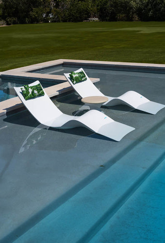 Two luxury chaise pool loungers with matching tropical headrest pillows and a side table.