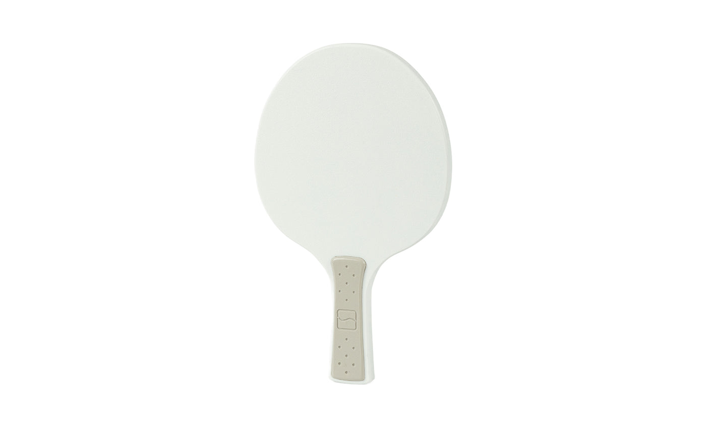 The Table Tennis Paddle by Ledge Lounger features a white plastic surface and a beige textured handle, resembling a traditional table tennis paddle, shown against a plain white background.