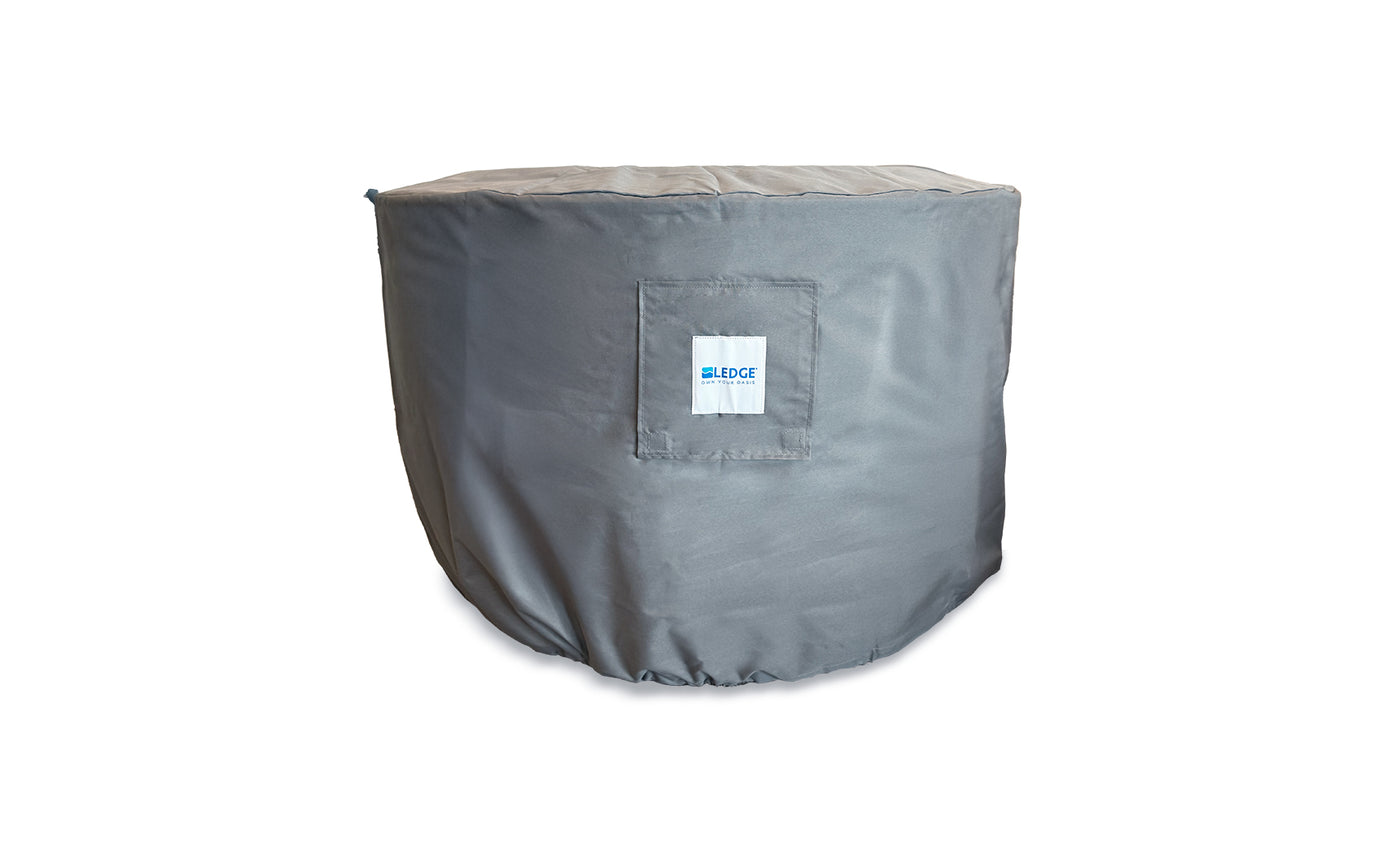 A gray Ledge Lounger Halo Firepit Cover with a square pocket, small white logo label, and adjustable drawstrings is fitted over a round object against a white background.