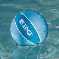 A blue and white basketball from the Ledge Basketball Set of 3 by Ledge Lounger floats on clear water, ready for a game with your Ledge Hoop.