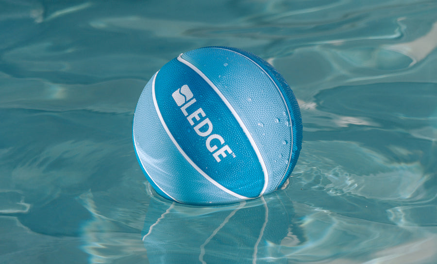 A blue and white basketball from the Ledge Basketball Set of 3 by Ledge Lounger floats on clear water, ready for a game with your Ledge Hoop.