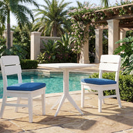 The Mainstay Bistro 5-Piece Set by Ledge Lounger, featuring two white chairs with blue cushions and a matching white table, is arranged on a stone patio beside the pool, surrounded by lush tropical plants, palm trees, and a pergola—an inviting setup that perfectly enhances your poolside lounge area.
