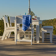 The Ledge Lounger Mainstay Dining 9-Piece Patio Set is showcased as a sample product, featuring a blue cloth draped over one chair and arranged on a wooden deck that overlooks scenic green trees and distant hills under a clear blue sky—making it an inviting addition to any outdoor space.