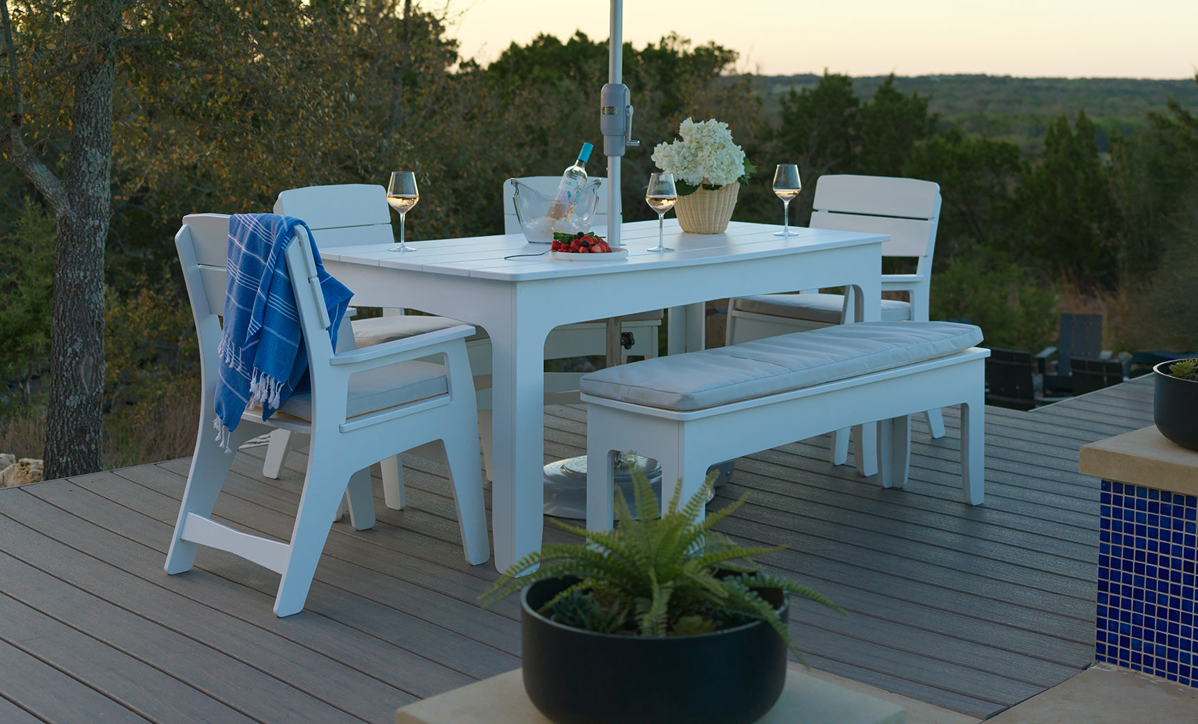 A sample product description: The Mainstay Dining 9-Piece Patio Set by Ledge Lounger is elegantly arranged with chairs, a bench, wine glasses, a wine bottle, flowers, and a blue towel on a deck surrounded by trees at sunset. This inviting scene perfectly showcases the patio set in an outdoor setting ideal for entertaining guests or relaxing with loved ones.