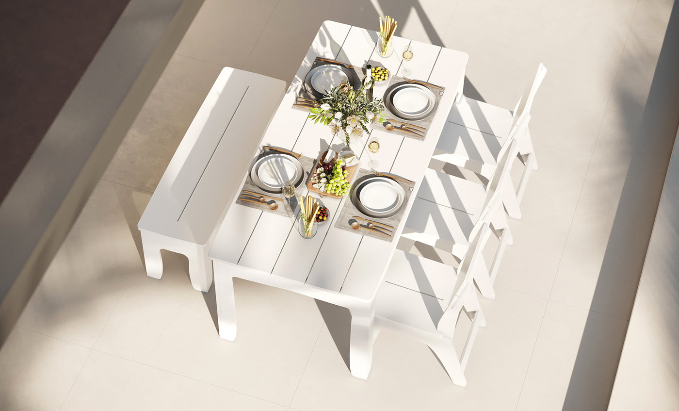 A bright, modern room features the Ledge Lounger Mainstay Dining 9-Piece Patio Set—a white dining table accompanied by three chairs and a bench, all set with plates, glasses, cutlery, a flower arrangement, grapes, and breadsticks—an inviting sample product that perfectly showcases contemporary dining elegance.