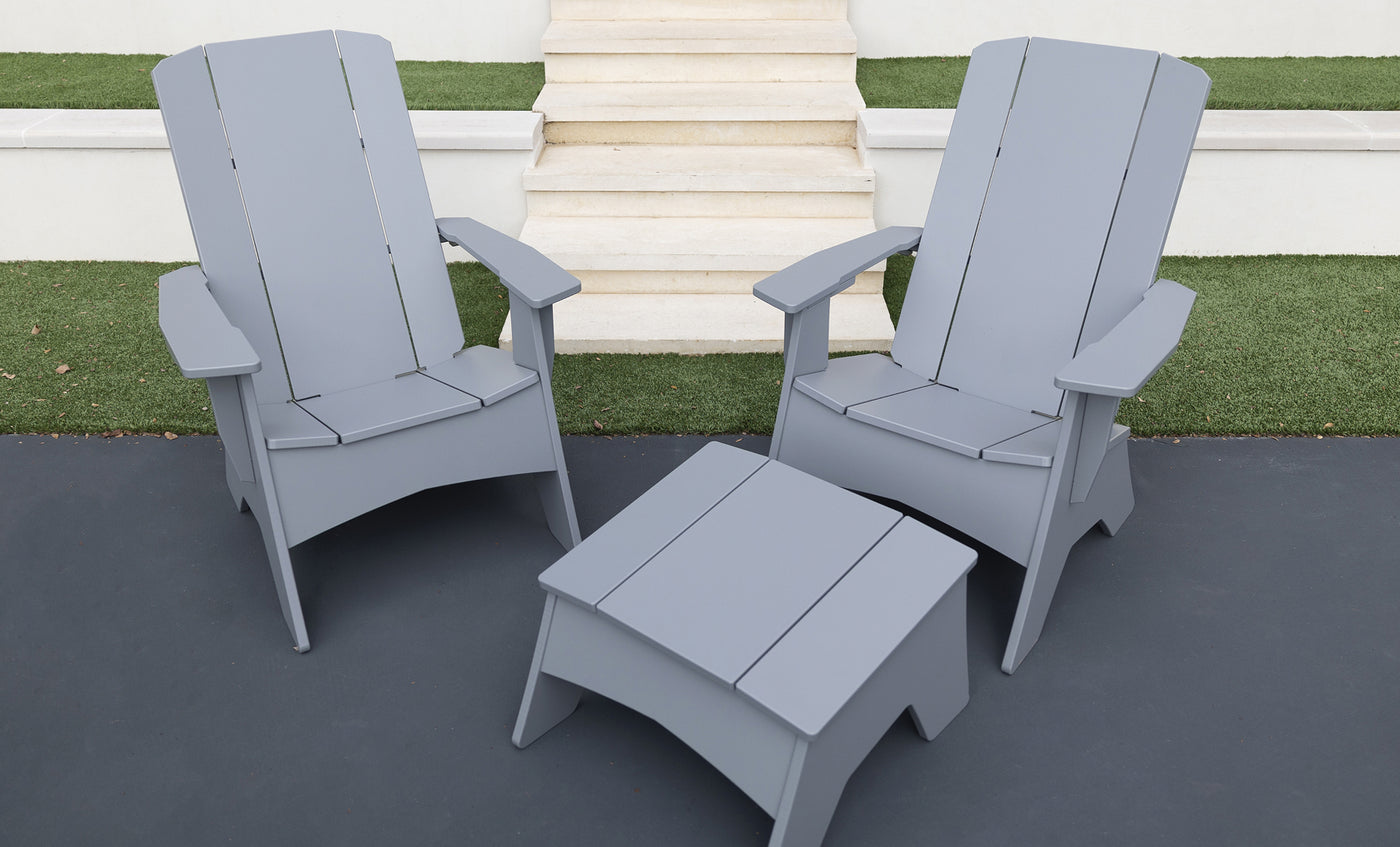 Two gray Ledge Lounger Mainstay Ultimate Adirondack chairs and a matching square table are set on a patio by white steps and artificial green grass.