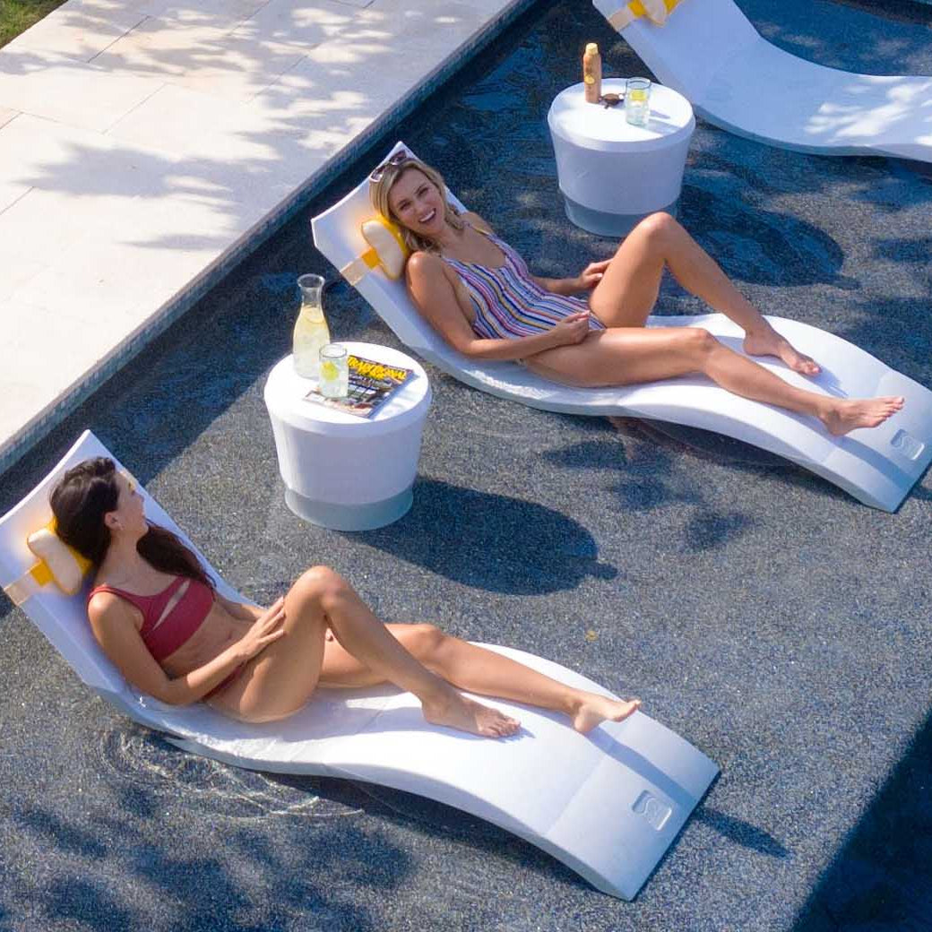 Girls smiling on in pool chaise loungers with matching headrest pillow and a side table.