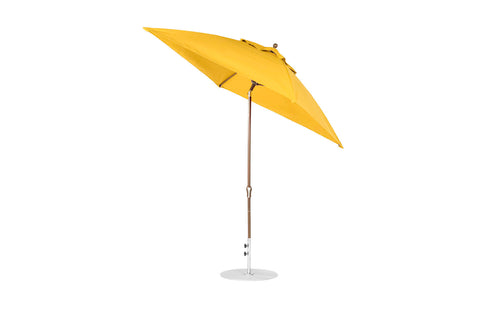 The Essential Fiberglass Umbrella by Ledge Lounger is a 7.5 octagon umbrella with a vibrant yellow canopy, elegantly tilted atop a wooden pole with a round silver base. Crafted from marine-grade fabrics, it offers wind resistance and ensures lasting shade and outdoor durability.
