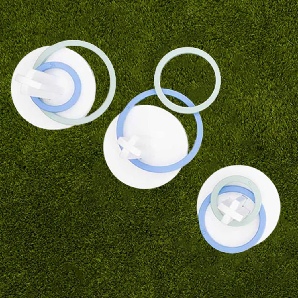Three white circular discs, featuring blue and white rings and crosses, are arranged on green grass. Their shadow effect adds depth for the ultimate backyard Ring Toss experience, presented by Ledge Lounger.