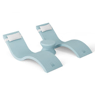 The Outdoor Paradise In-Pool Furniture Bundle by Ledge Lounger includes two aqua blue, wave-shaped chaise loungers with white headrests and a central circular table, offering a modern and sleek design ideal for pool ledge relaxation against a simple white background.
