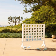 The Ledge Lounger Four In A Row stands on a patio by the pool, surrounded by lush greenery and trees, with a distant city skyline under a clear blue sky.