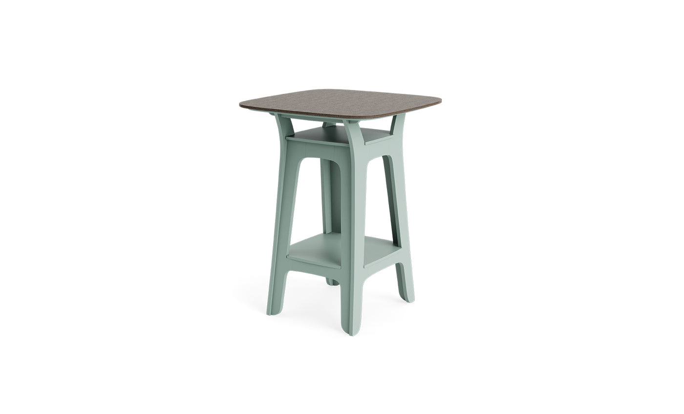 The Ledge Lounger Haven Hightop Table features a square grey tabletop, light green legs, a storage shelf, and a minimalist design—ideal for enhancing any outdoor space against a plain white background.