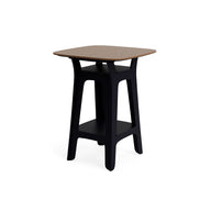 The Haven Hightop Table by Ledge Lounger features a square wooden top, black angled legs, and a lower storage shelf—a modern side table ideal for enhancing your outdoor space.
